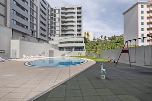 Un área de piscina en la azotea con sillones de descanso, un conjunto de columpios y una escalera que sube a un nivel superior.