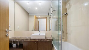 A modern bathroom with a glass-enclosed shower, a sink with a marble countertop, and wooden cabinets. - Blue and Gold Sunset by Homie (Funchal)
