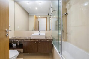A modern bathroom with a glass-enclosed shower, a sink with a marble countertop, and wooden cabinets.