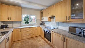 A modern kitchen with wooden cabinets, a built-in oven, a microwave, and a window providing natural light. - Host & Stay | Blue Sky Cottage (Whitby)