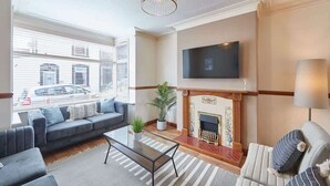 A living room with a sofa set, a fireplace, a television mounted on the wall, and a potted plant. - Host & Stay | Blue Sky Cottage (Whitby)