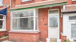 A red brick house with a white front door, a large window with white frames, and a small porch area. - Host & Stay | Blue Sky Cottage (Whitby)