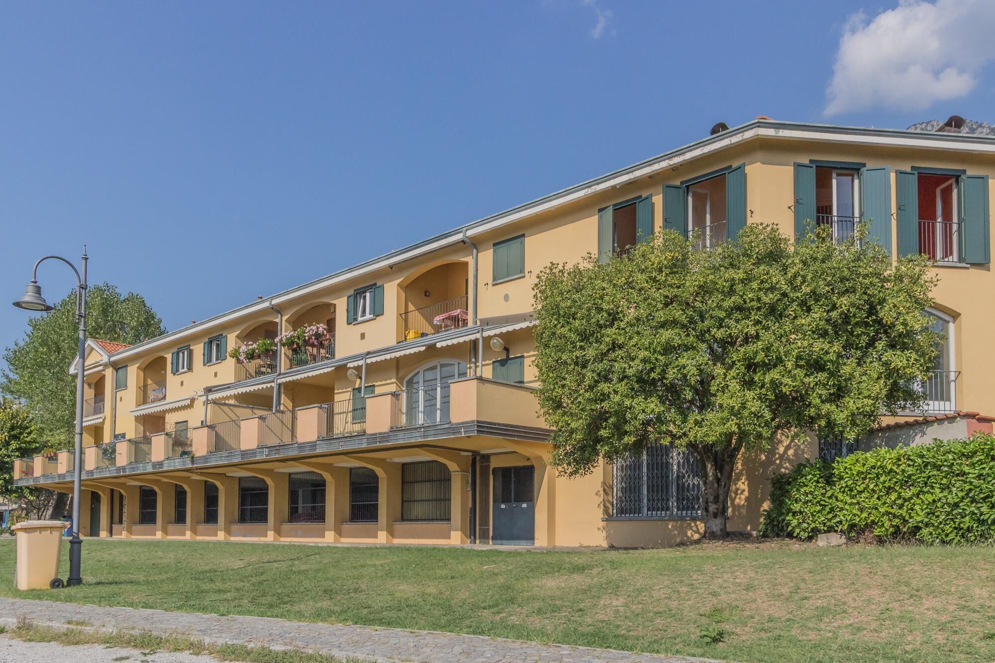 A multi-story building with balconies, a tree in front, and a clear blue sky.