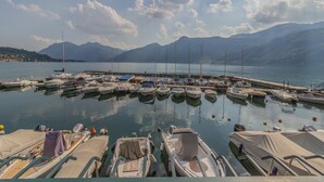 A marina with boats docked, calm water, and mountains in the background.