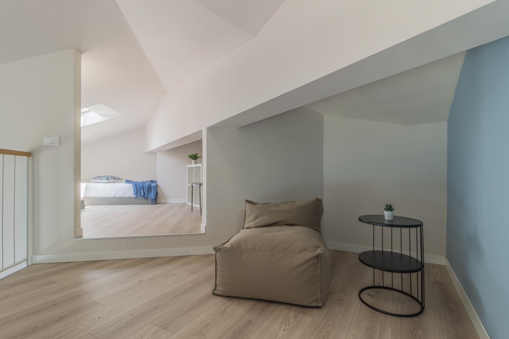 Un'ampia camera da letto mansardata con una grande finestra, un letto, un divano color beige e un piccolo tavolino rotondo.
