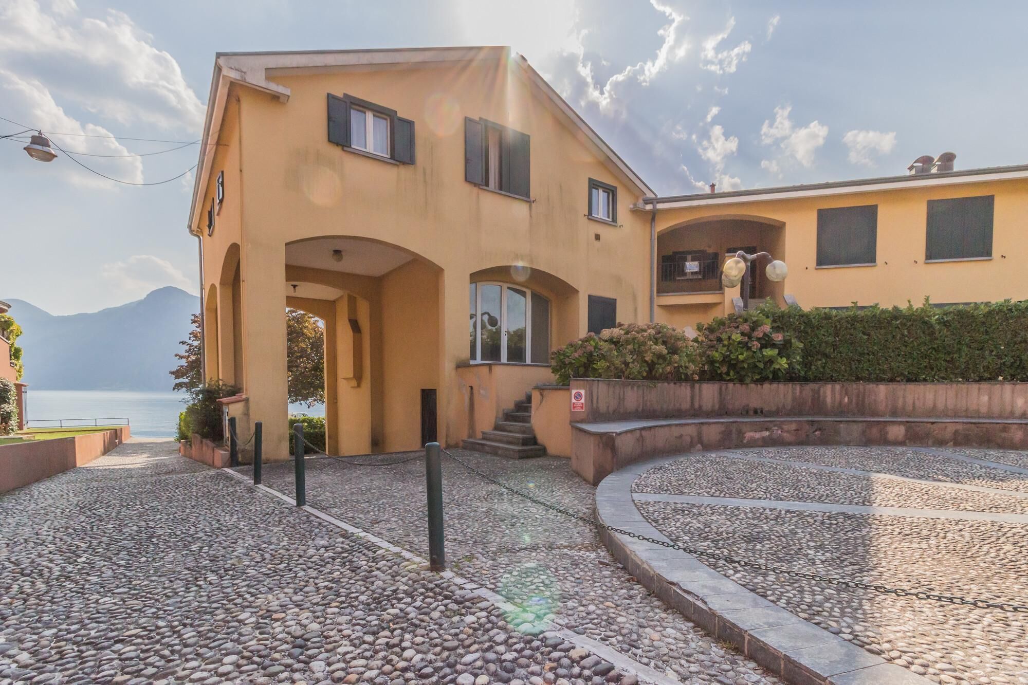A building with a yellow facade, a stone-paved entrance, and a view of the water.