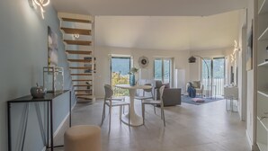A spacious living area with a staircase, a dining table with chairs, a sofa, and a view of the outdoors.
