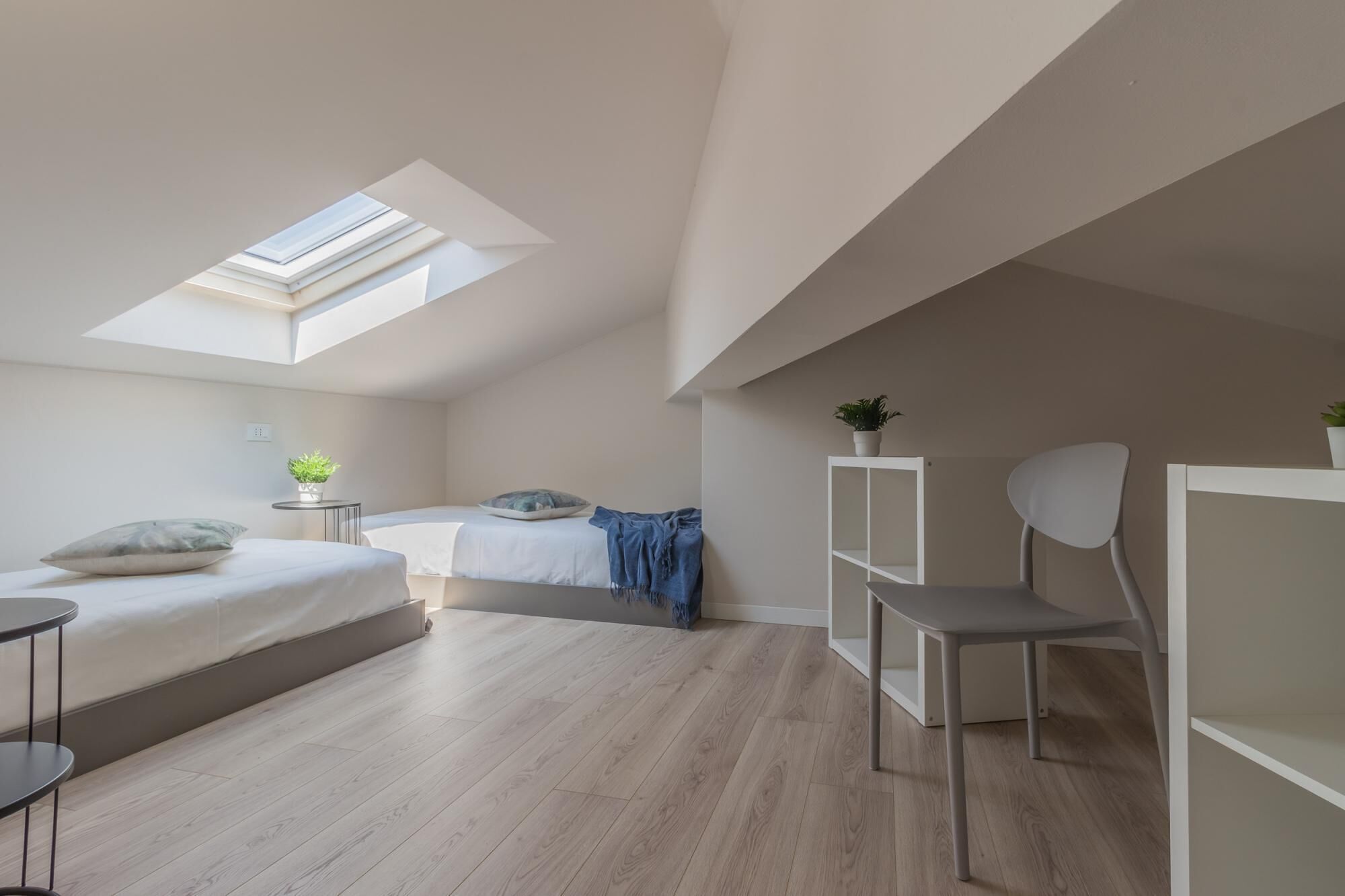 A modern bedroom with a skylight, a bed, a desk, and a chair.