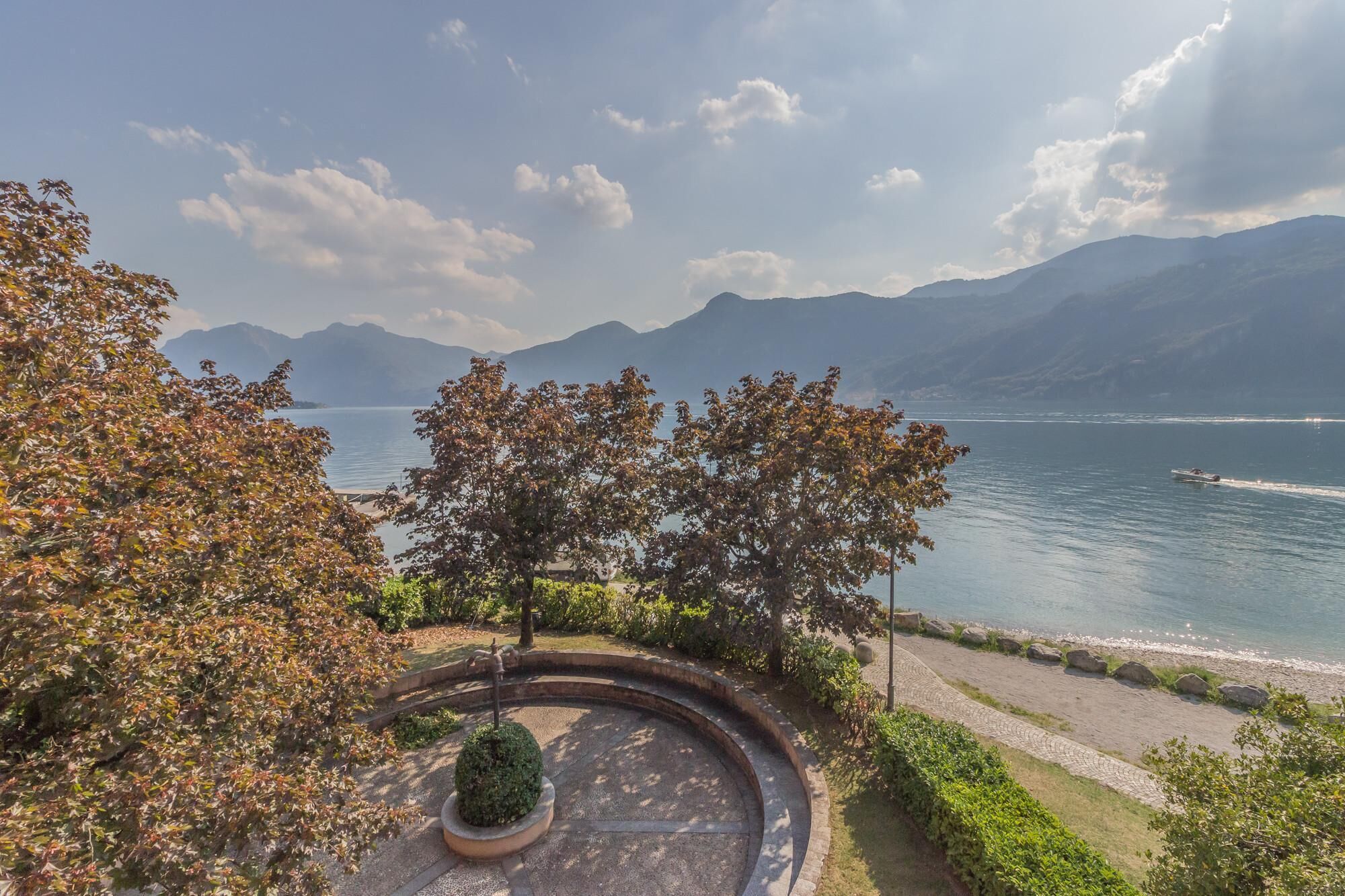 Un espace paysager comprenant un jardin circulaire, un sentier et une vue sur un lac, avec des montagnes en arrière-plan.