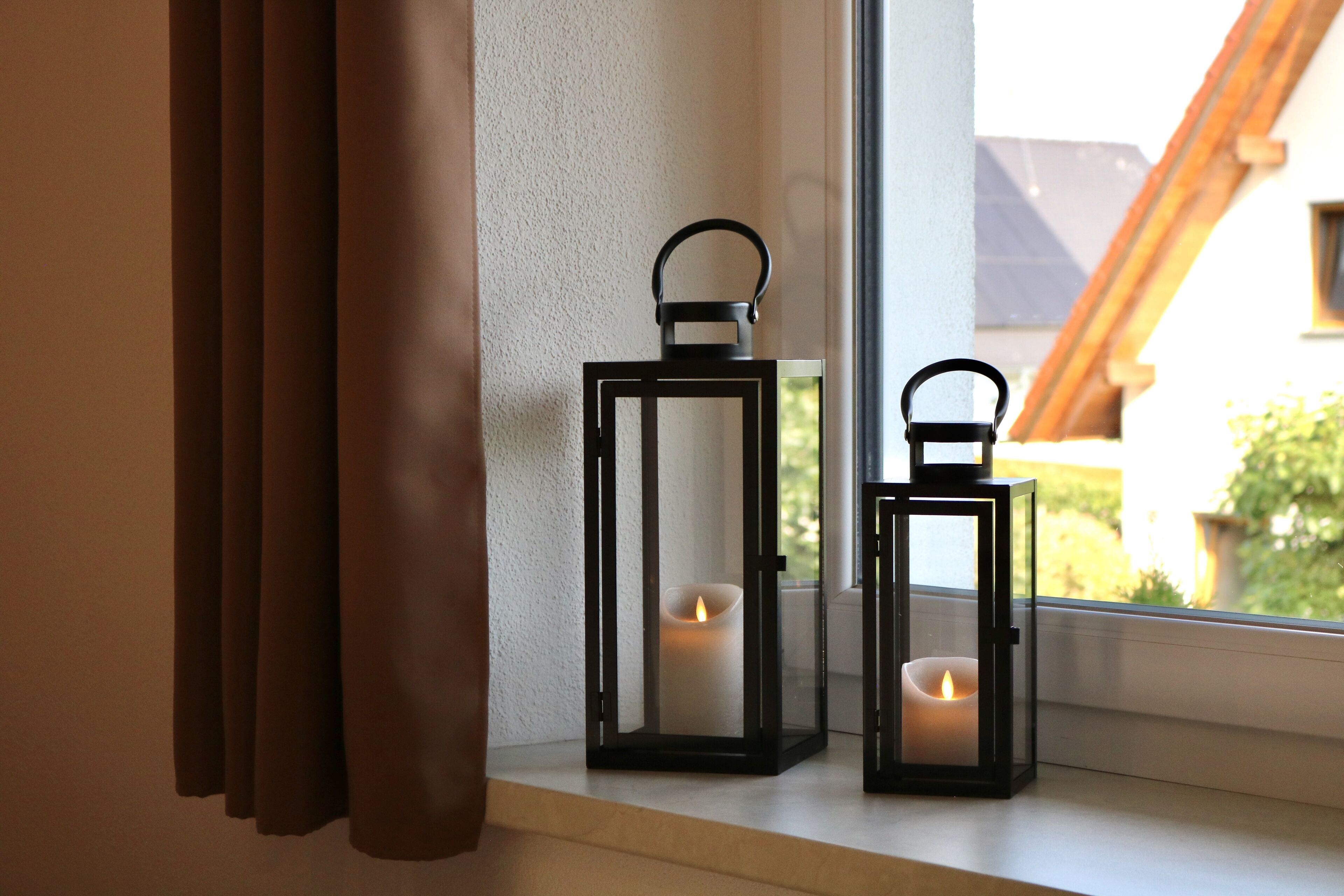 Two black lanterns with candles on a windowsill.