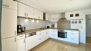 A modern kitchen with white cabinetry, stainless steel appliances, and wooden flooring. - Modern vacation apartment in the Allgäu (Erkheim)