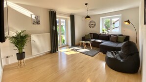 A modern living room with a sofa, a coffee table, a black bean bag, a potted plant, and a large window. - Modern vacation apartment in the Allgäu (Erkheim)