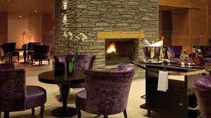 A lobby with a stone fireplace, purple upholstered chairs, and a bar area with glasses and bottles. - Lagrange Vacances L'Alpenrose (Huez)