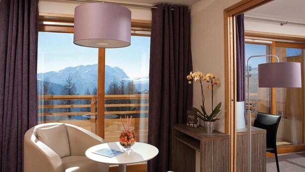 A modern room with a view of mountains, a sofa, a small table with a glass, and a vase of flowers. - Lagrange Vacances L'Alpenrose (Huez)