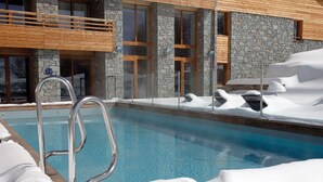 A pool with a metal ladder, surrounded by snow, in front of a stone building with large windows and a wooden balcony. - Lagrange Vacances L'Alpenrose (Huez)