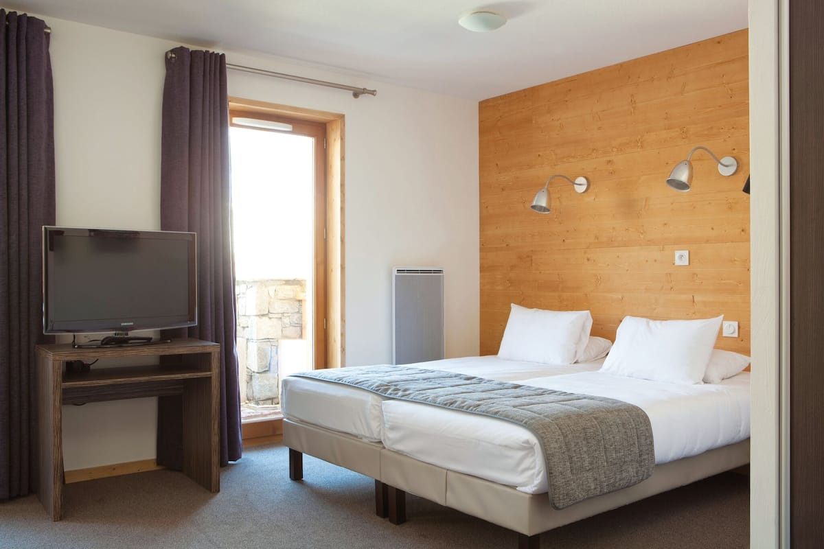 A hotel room with a bed, a TV on a wooden stand, a stone wall, and a wooden ceiling.