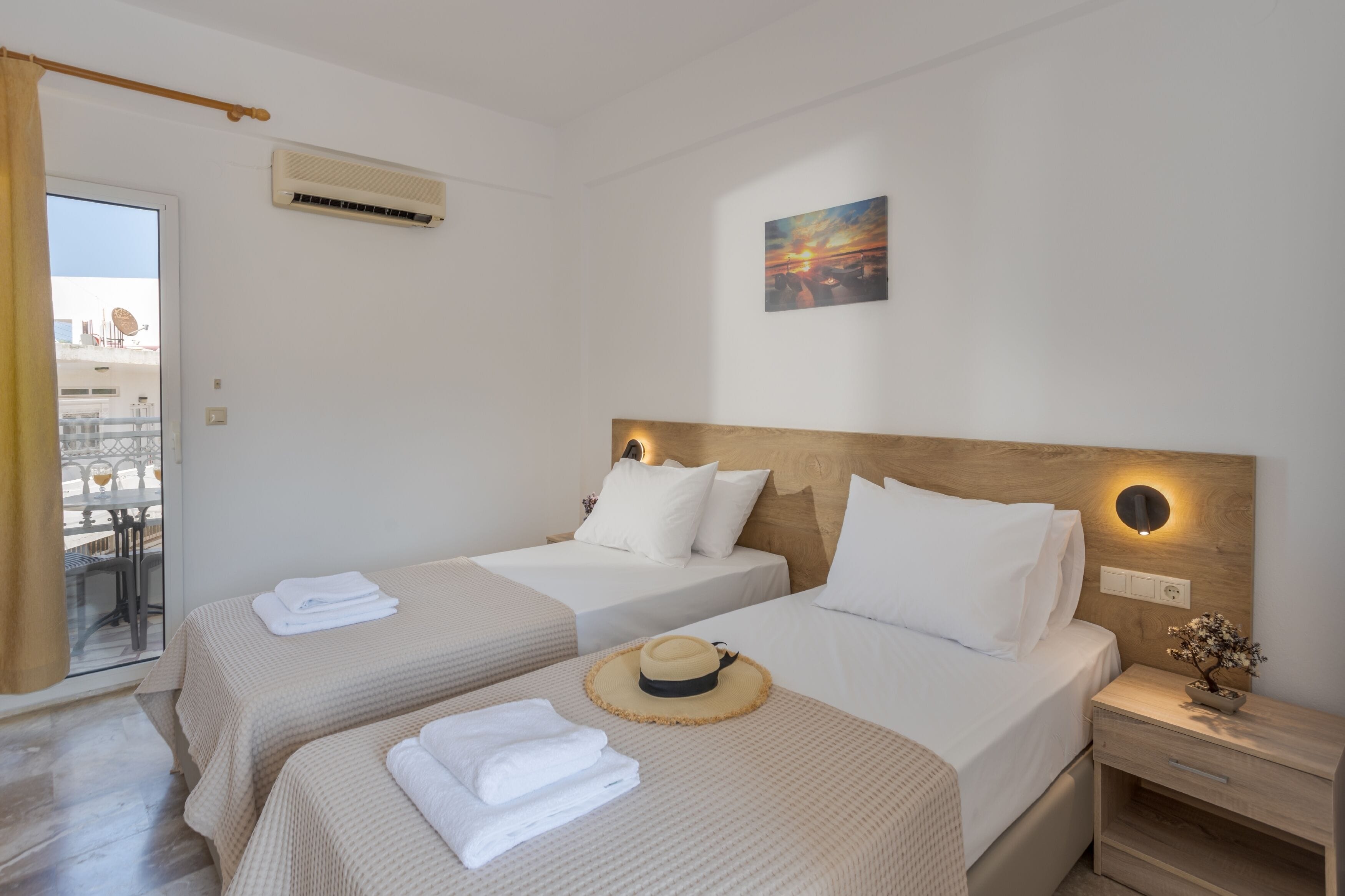 Une chambre d’hôtel avec deux lits, une tête de lit en bois, un tableau, un appareil de climatisation et une vue sur l’extérieur.