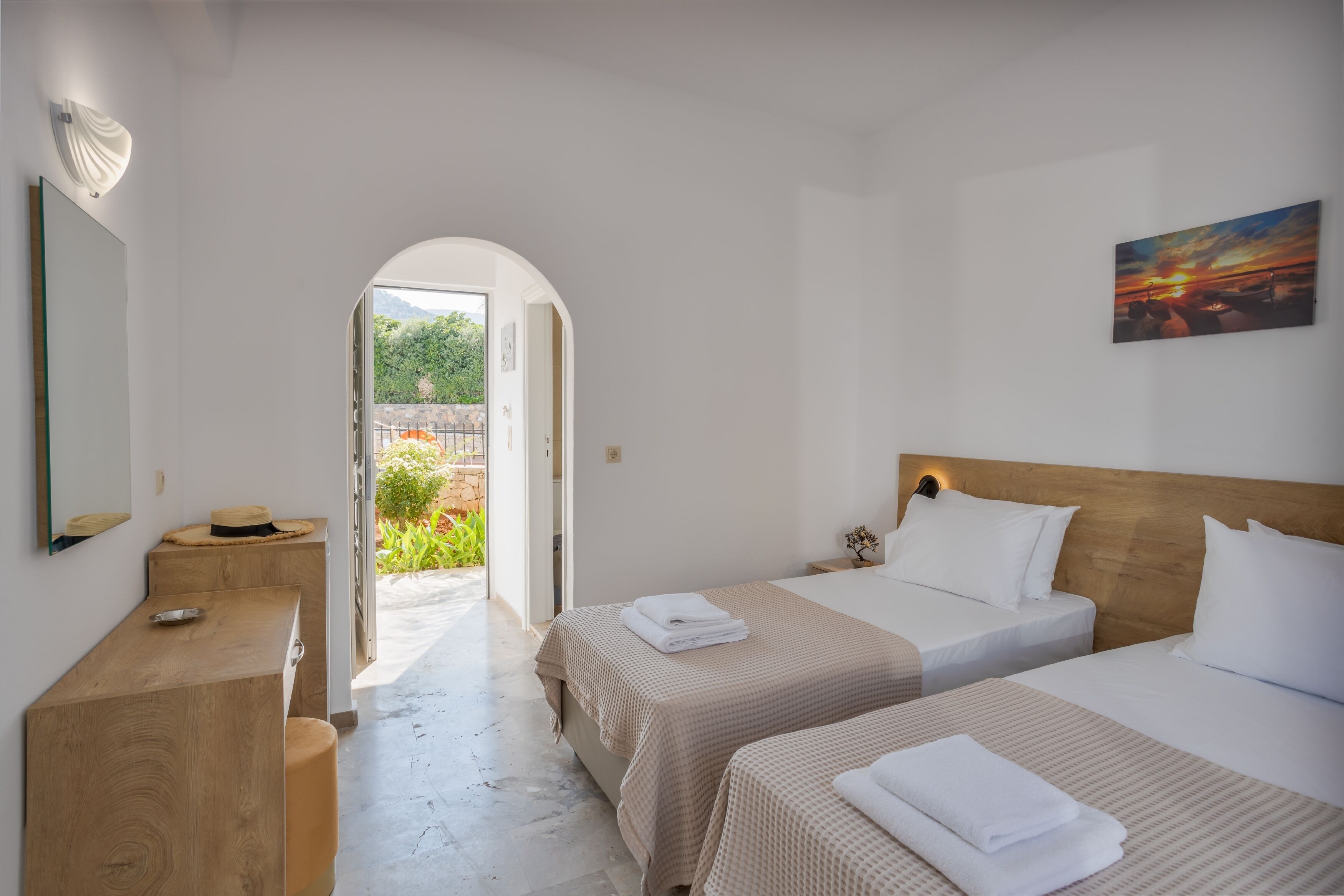 A hotel room with two beds, a wooden desk, a mirror, and a painting.
