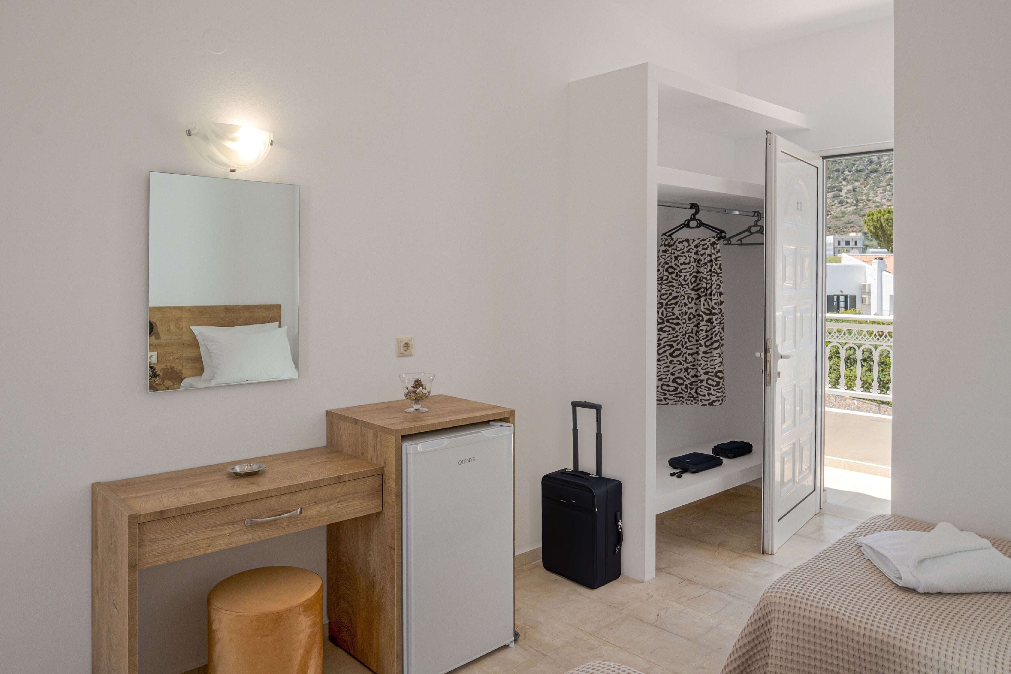 Une chambre à coucher comprenant un lit, un bureau, un petit réfrigérateur, une valise et une salle de bain avec un rideau de douche.