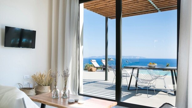 A modern living room with a large sliding glass door leading to a balcony with a pool and lounge chairs. - Villa Dimelisa - Modern Villa with breathtaking views of the Ionian Sea (Argostoli)