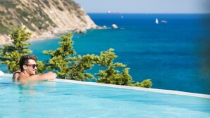 A man relaxing in a clear blue infinity pool with a view of the sea and a rocky coastline. - Villa Dimelisa - Modern Villa with breathtaking views of the Ionian Sea (Argostoli)
