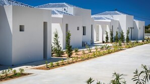 A row of modern white buildings with tiled roofs and small windows, surrounded by a landscaped garden with young trees. - Villa Dimelisa - Modern Villa with breathtaking views of the Ionian Sea (Argostoli)
