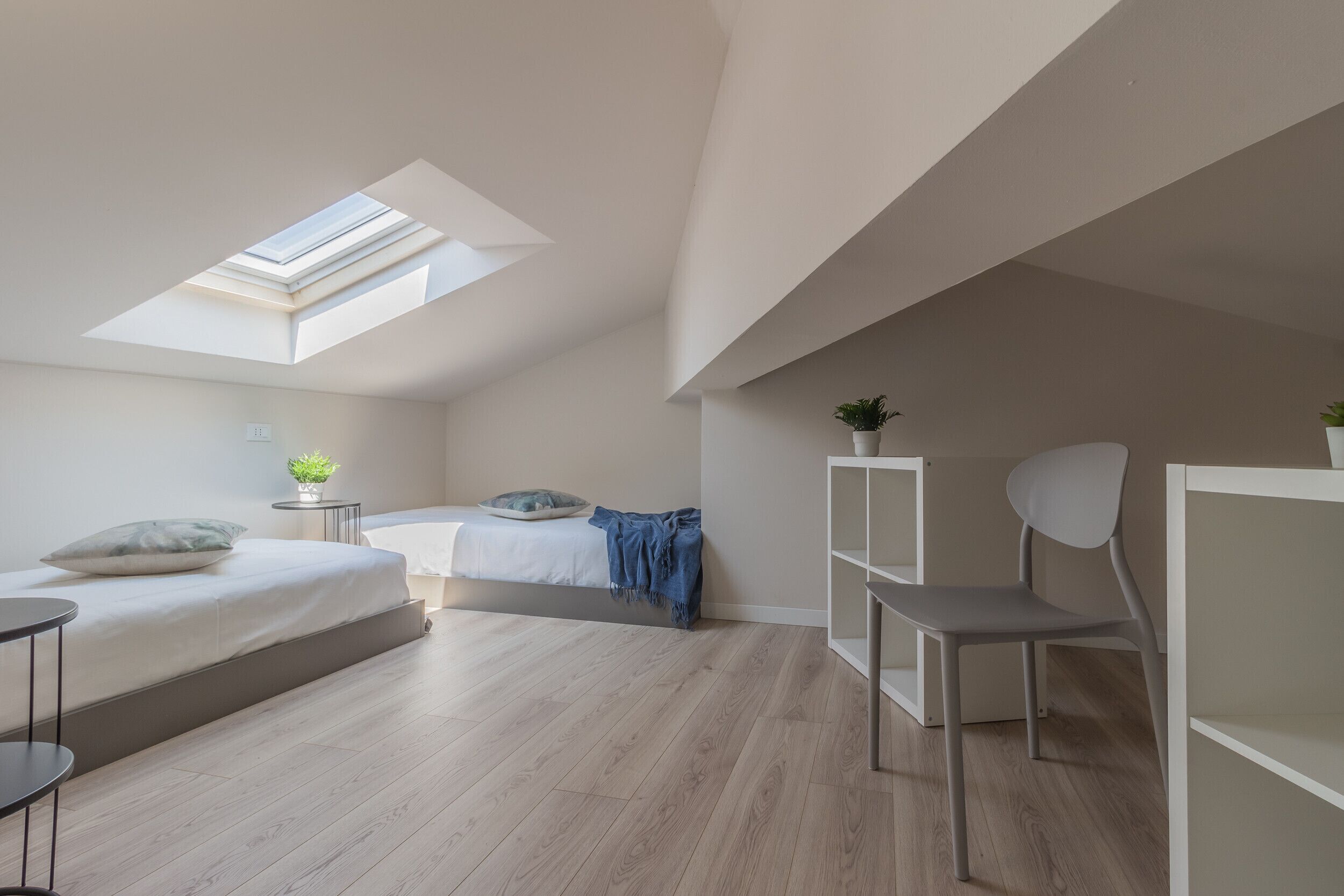 A modern bedroom with a skylight, a bed, a desk, a chair, and a small plant.