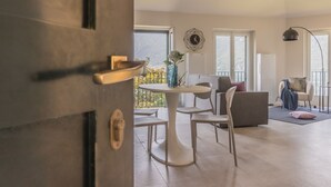An open door leading to a living area with a dining table, chairs, a sofa, and a balcony with a view. - Sunset View Lierna_varennaholidays (Lierna)