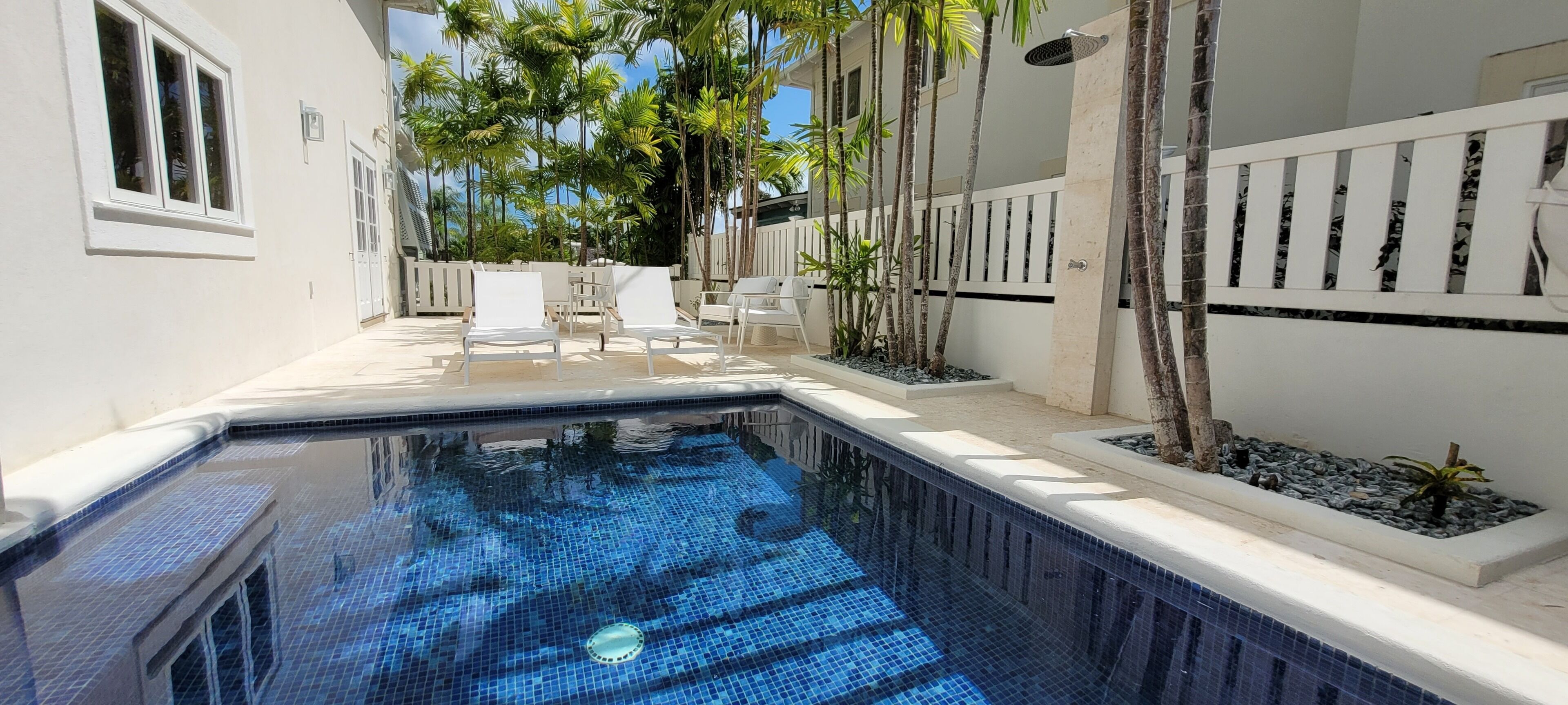 A swimming pool with tiled flooring, surrounded by white walls and a white fence.