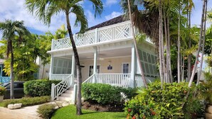A two-story building with a white exterior, a covered porch, and a small garden area with palm trees and shrubs. - Beautiful  4BR villa w/pool in St James, Porters.  5 min walk to gorgeous beach. (Porters)