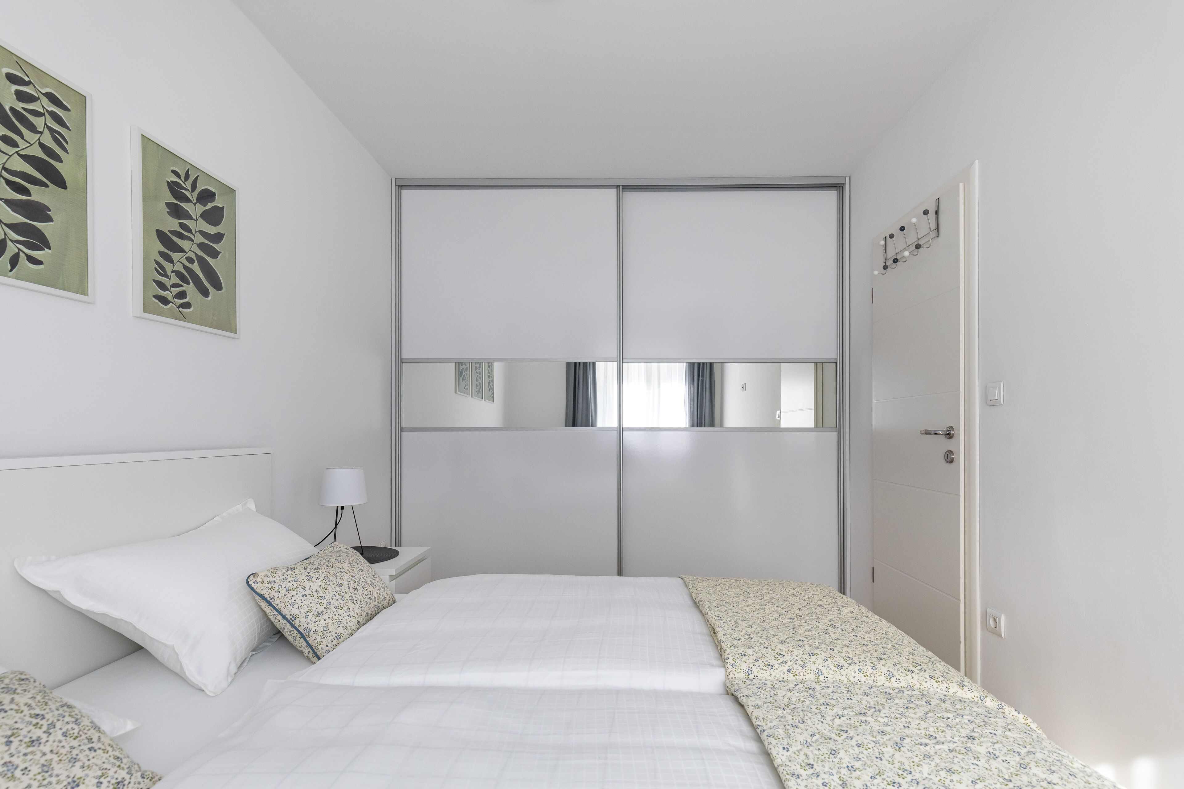 Ein Schlafzimmer mit Bett, Nachttisch, Lampe, Kleiderschrank und zwei Wandbildern.