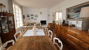 Ein Esszimmer mit Holztisch, weißen Stühlen, einem Schrank und einem Gemälde an der Wand.