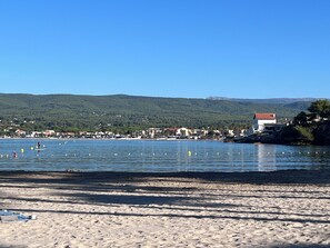 A beach with a clear view of the sea, a sandy shore, and a town in the background.
