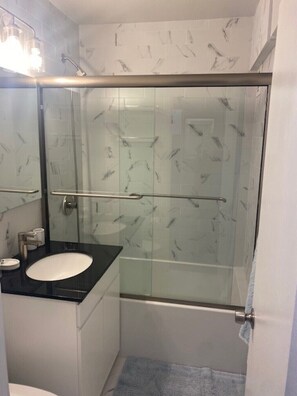 Bathroom features a glass-enclosed shower, sink, and mirror.