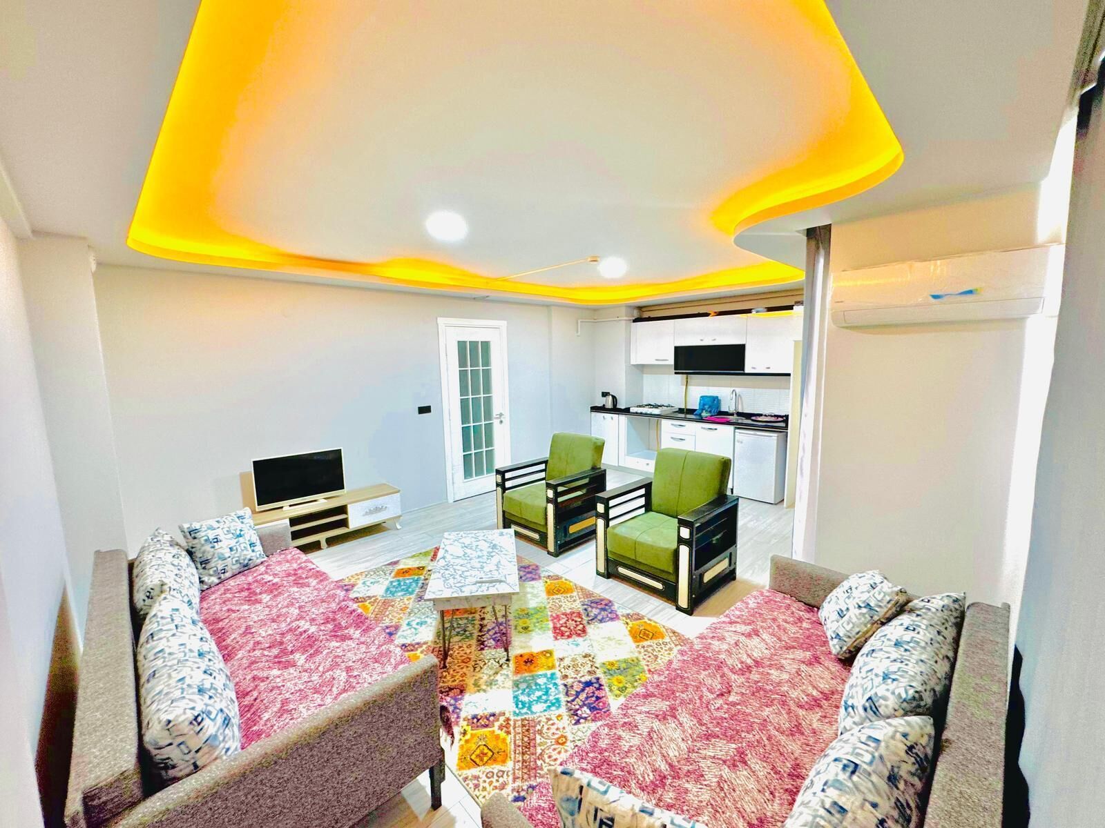 A compact living space with a kitchenette, a television, and a colorful rug.