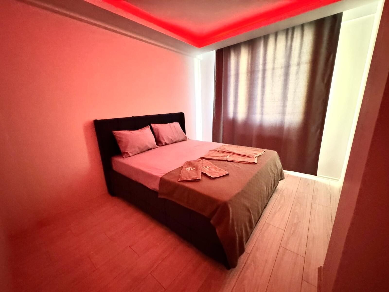 A modern bedroom with a bed, a window with curtains, and a red accent wall.