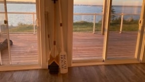 Ein Zimmer mit großen Schiebeg lassüren, die auf eine Holzdielen-Terrasse mit Blick auf das Wasser führen.