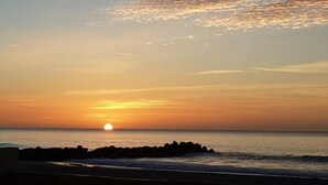Un coucher de soleil sur l’océan, avec une côte rocheuse.