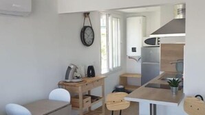 Une cuisine compacte avec une table à manger en bois et quatre tabourets, un petit îlot de cuisine et une horloge murale.