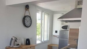 Une cuisine de taille réduite avec un îlot central en bois, des tabourets de bar, un four à micro-ondes et une horloge murale.