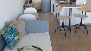 Un espace de vie compact comprenant un canapé, un petit coin cuisine avec un four à micro-ondes et un réfrigérateur, ainsi qu’une table à manger avec des chaises.