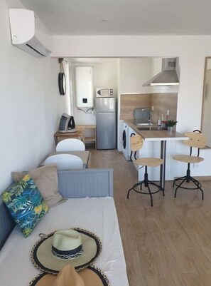 Um espaço de estar compacto com sofá, cozinha compacta incluindo micro-ondas e frigorífico, e mesa de jantar com cadeiras.