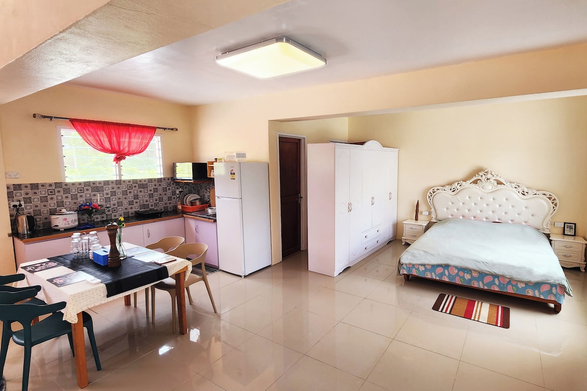 A compact hotel room with a kitchenette, a bed with a patterned bedspread, and a small dining area.