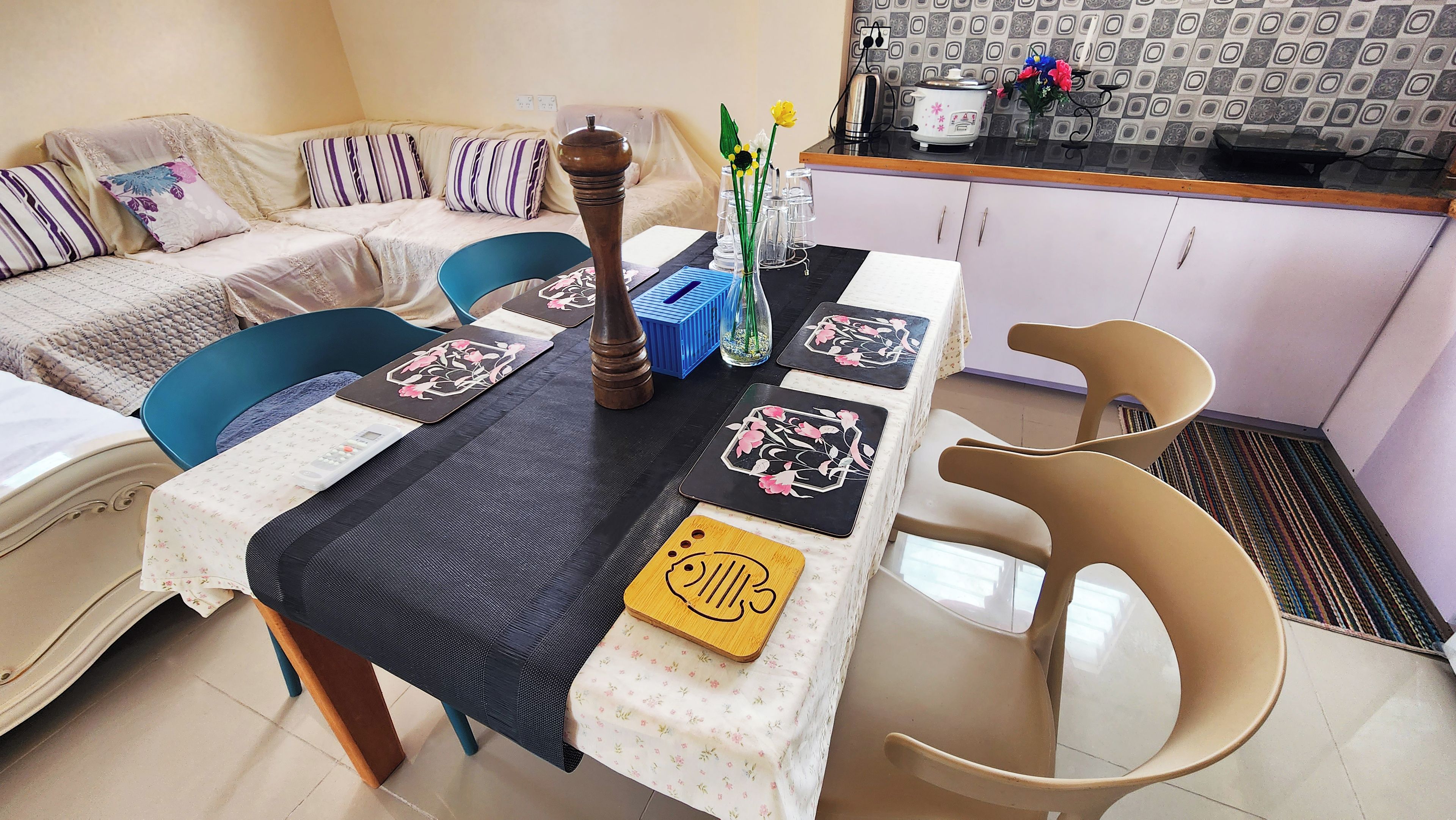 Un comedor con una mesa dispuesta para cuatro personas, un sofá y una cocina al fondo.