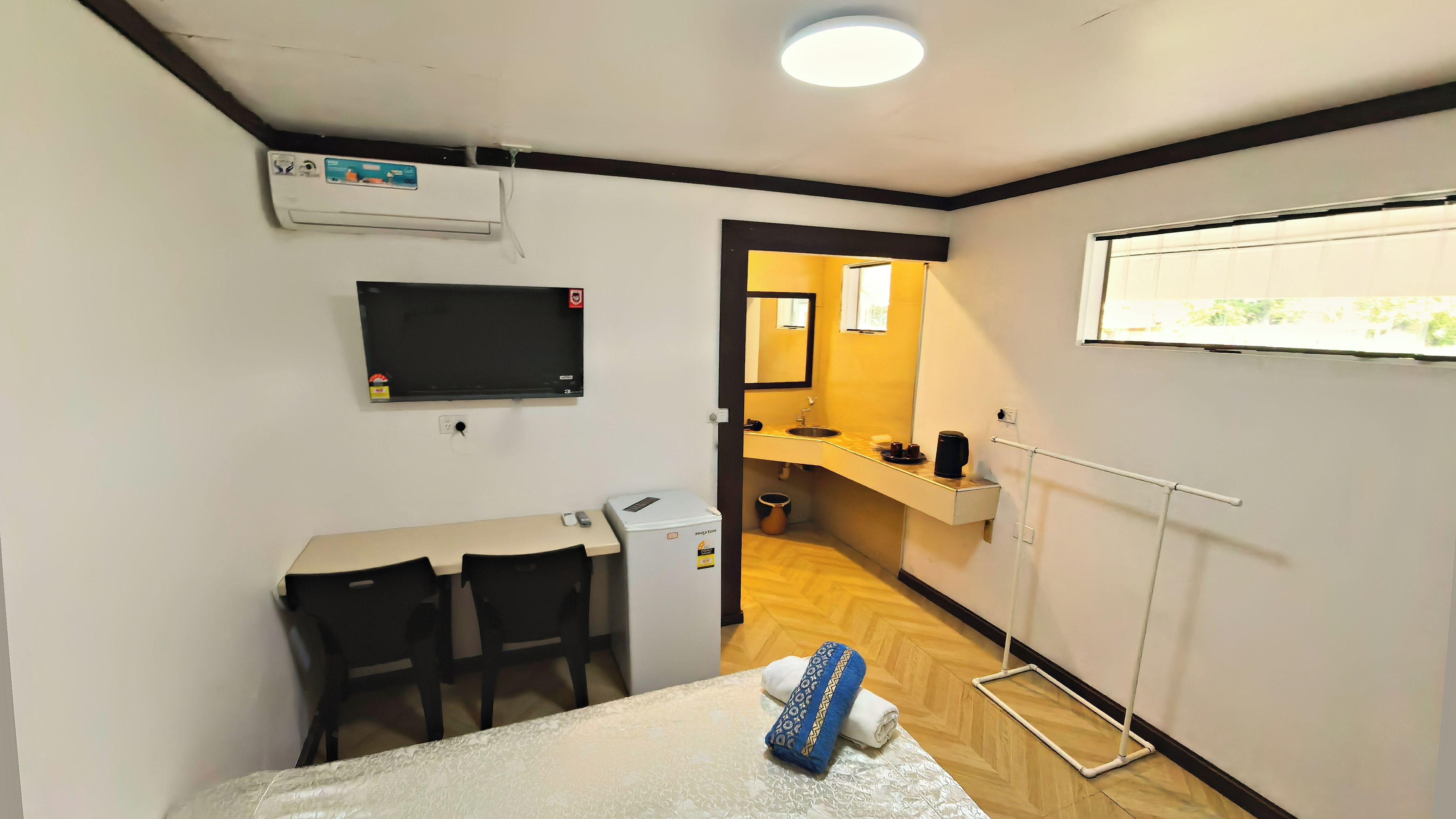 A hotel room with a bed, a desk with chairs, a television, a small kitchenette, and a window.