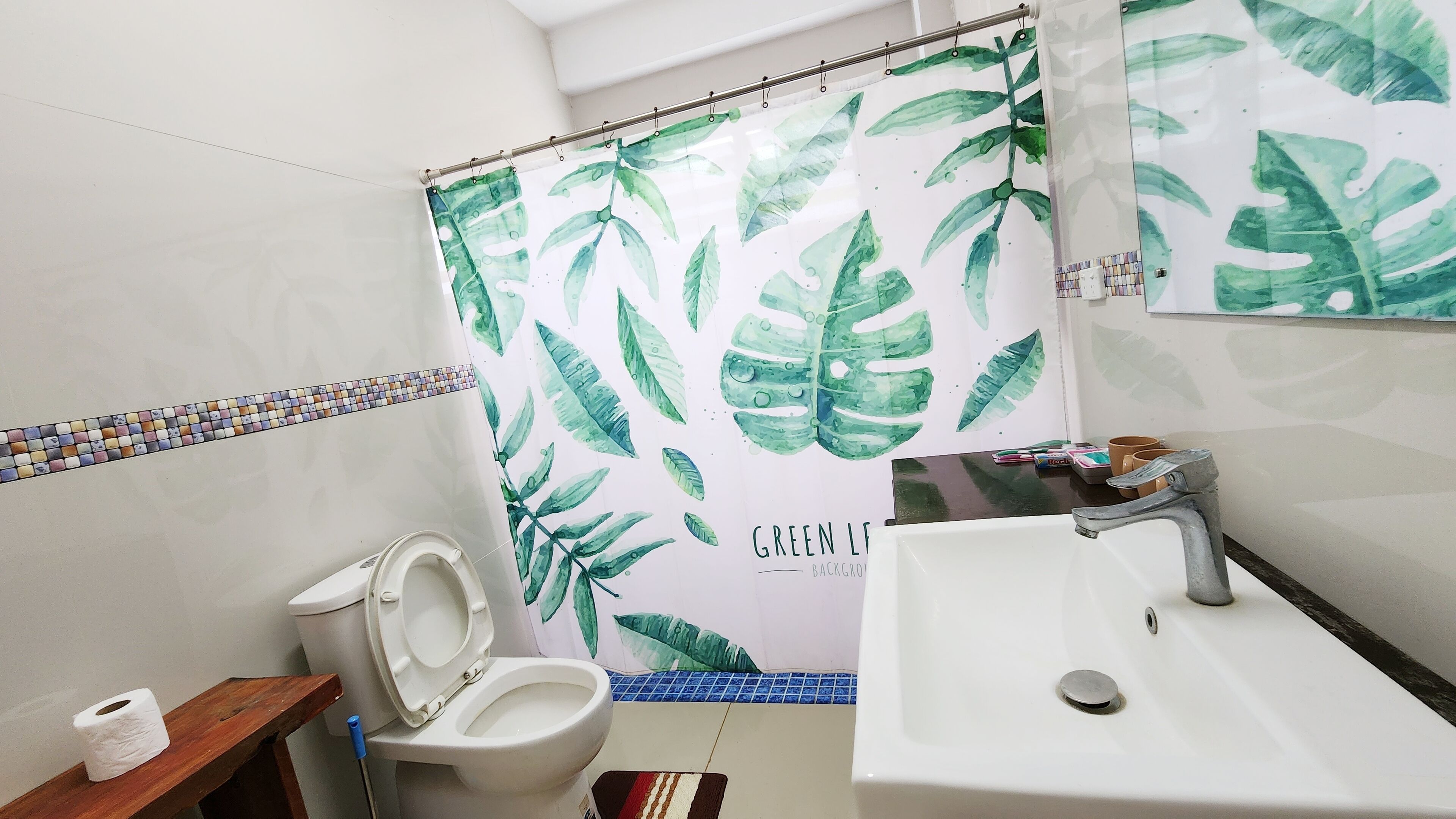 A bathroom with a toilet, sink, and shower curtain with a green leaf pattern.