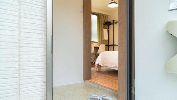 A hotel room entrance with a wooden floor, a bed with a white cover, a chair, and a small table. - K HOUSE - E JOY INN Okubo Branch (Tokyo)
