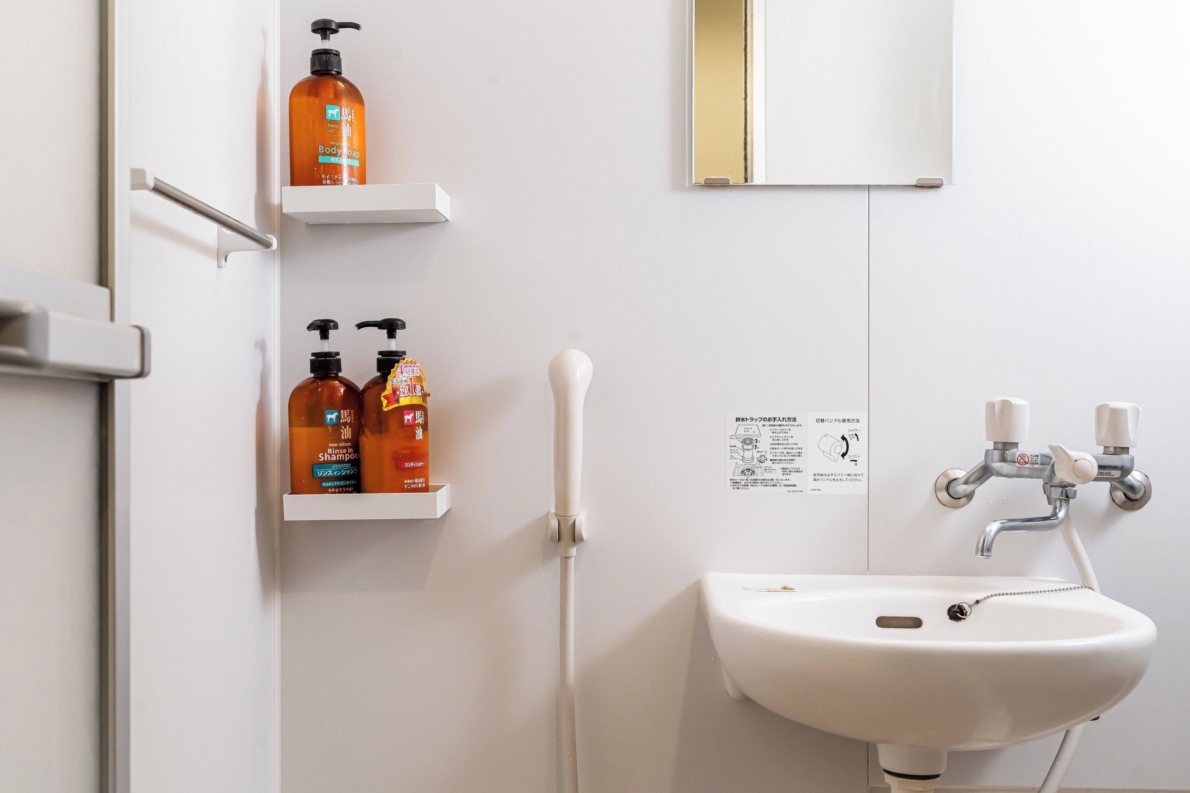 A bathroom with a white sink, two shelves with toiletries, a hand dryer, and a mirror.