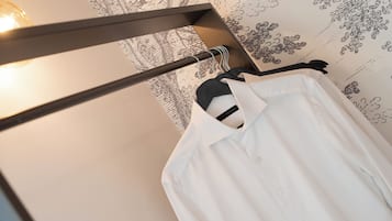 Una camisa blanca colgada en un perchero en una habitación con papel tapiz estampado y una lámpara visible.
