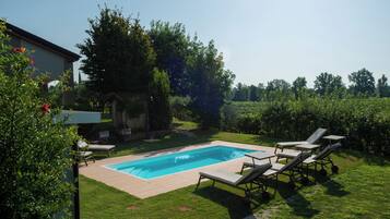 Una piscina rettangolare con bordo in legno, circondata da un prato e alberi.